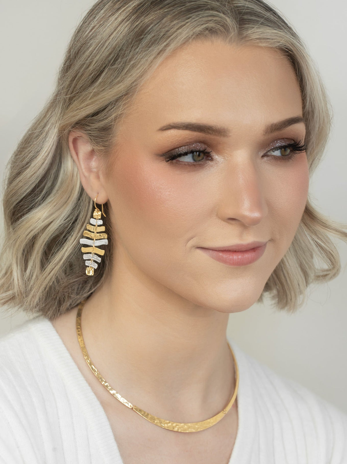 Woman wearing gold earrings and necklace against a neutral background
