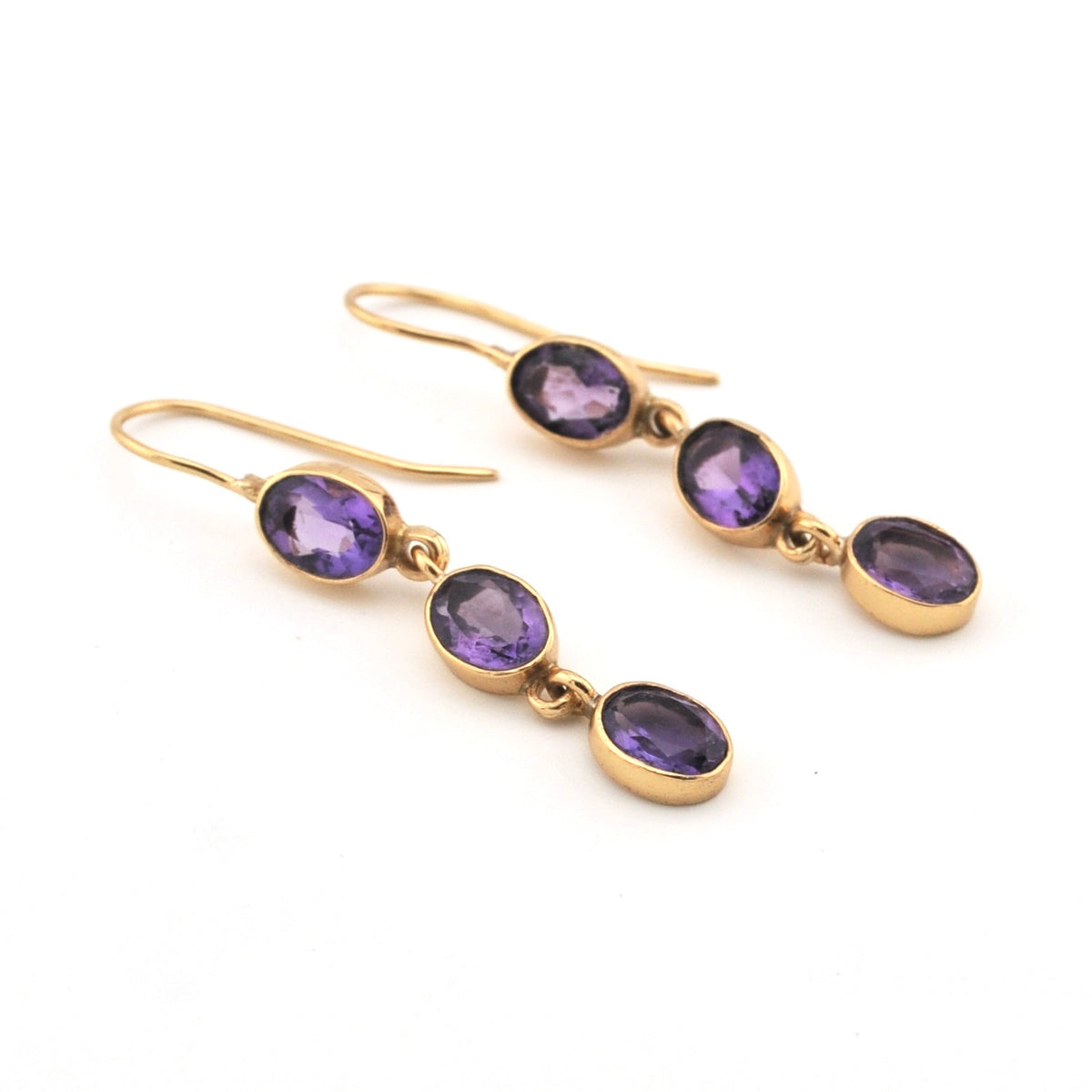 Gold earrings with purple gemstones on a white background