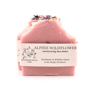 Pink soap bar with dried flowers on top and a label reading 'Alpine Wildflower' on a white background.