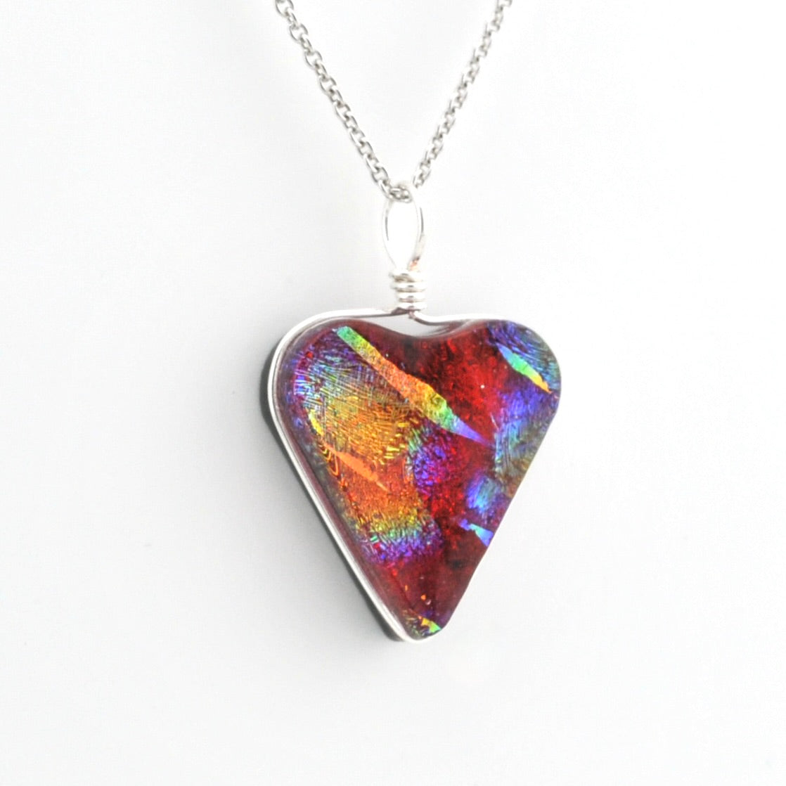 A heart-shaped glass pendant necklace with an iridescent, opalescent pattern showing red, orange, green, and blue colors, set in a silver-tone bezel on a silver chain against a white background.
