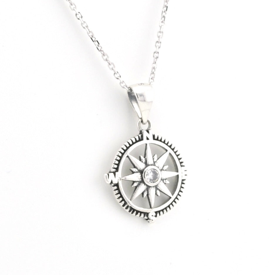 A silver compass pendant necklace with a central clear gemstone, shown on a delicate silver chain against a plain white background.