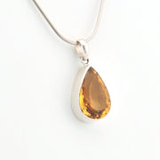 Teardrop-shaped citrine pendant on a silver chain against a white background