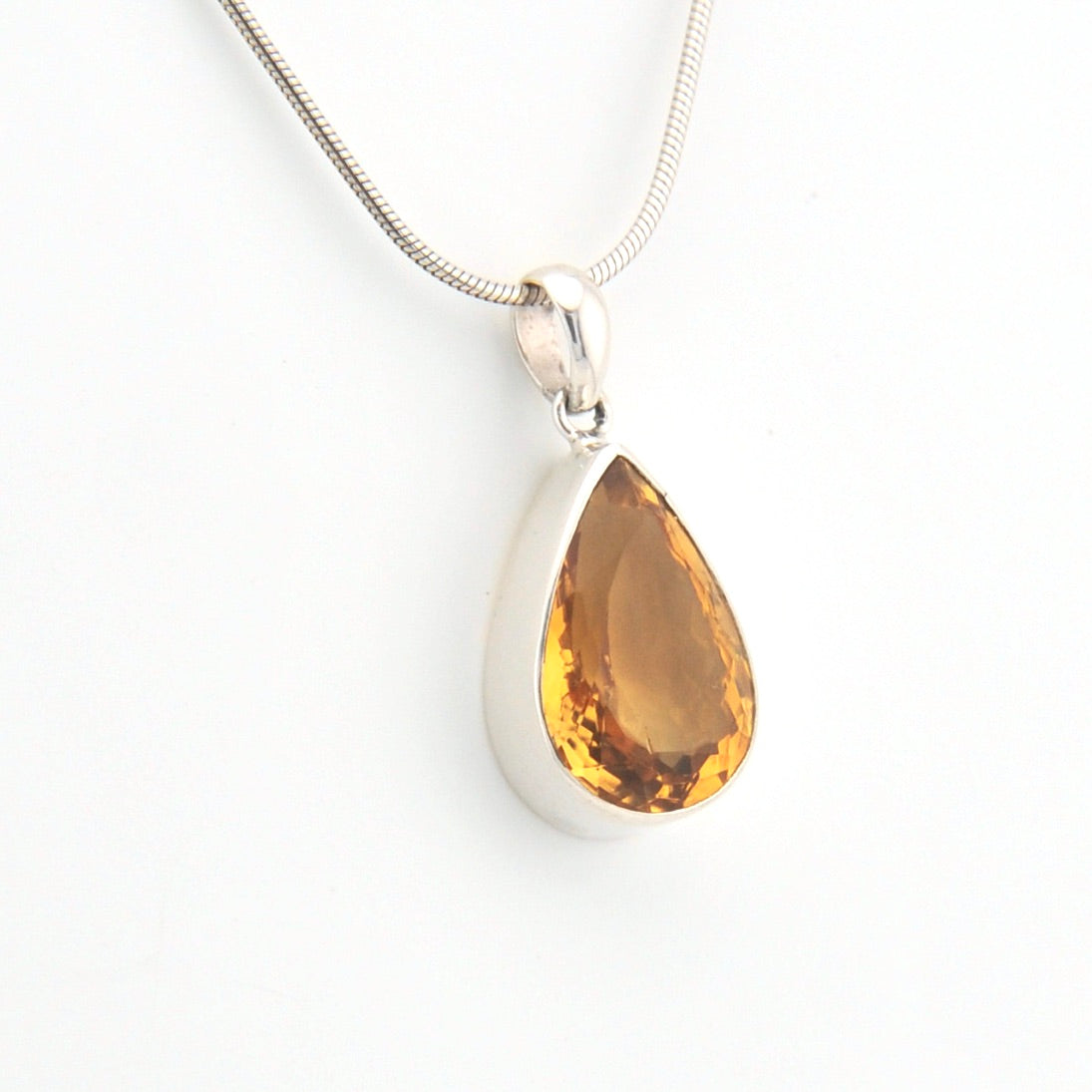 Teardrop-shaped citrine pendant on a silver chain against a white background