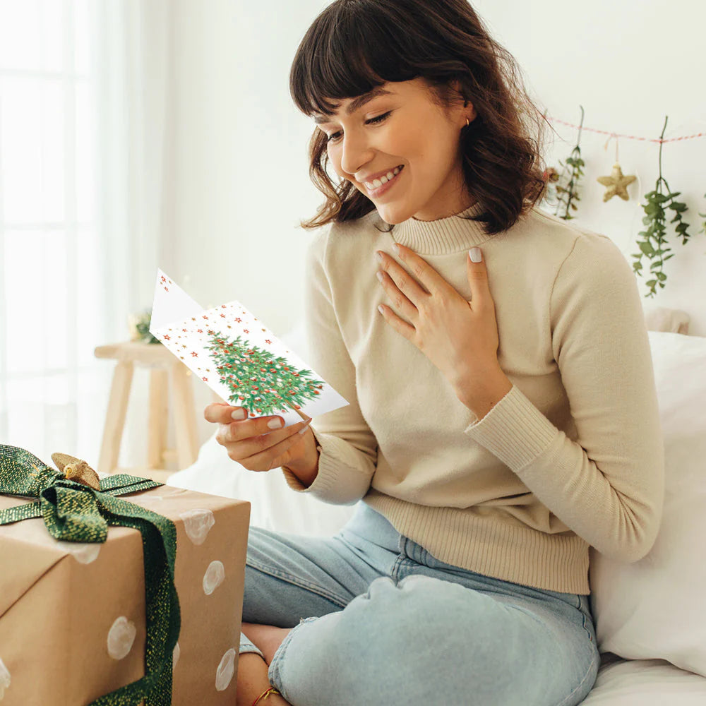 Woman opening a gift with a smile, surrounded by festive decorations.