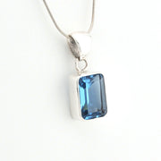 Blue gemstone pendant on a silver chain against a white background