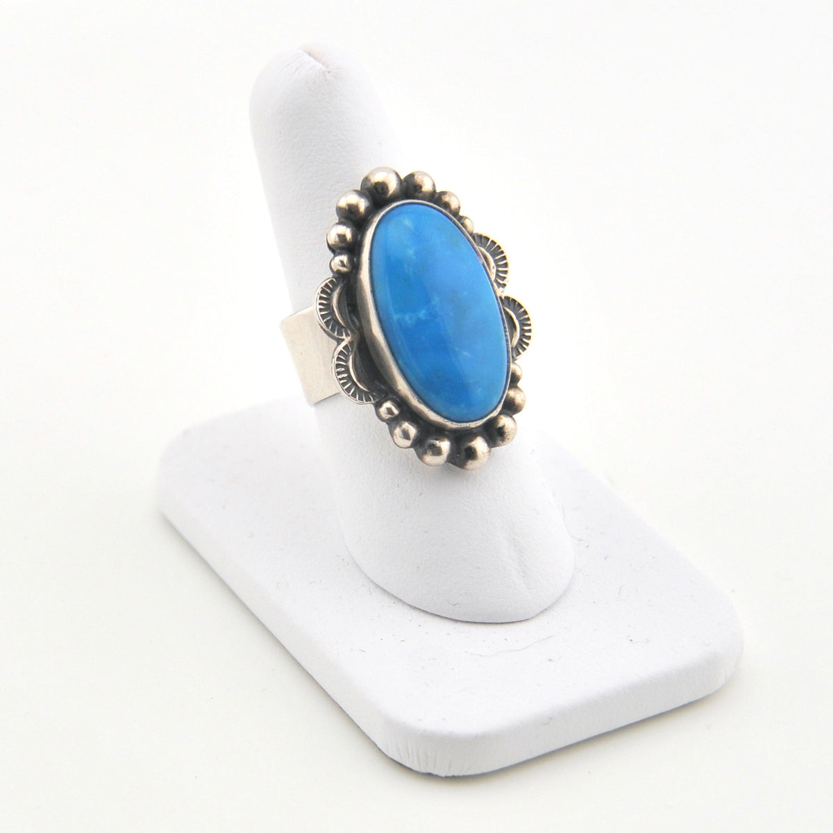 Blue stone ring with silver band on a white stand