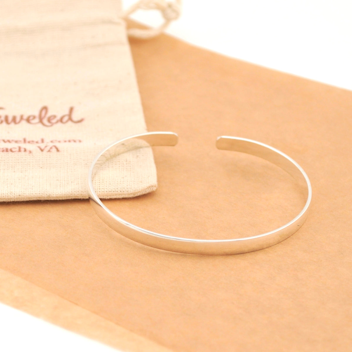 Silver bracelet on a beige surface with a branded pouch in the background