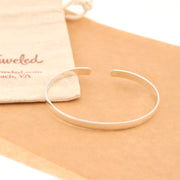 Silver bracelet on a beige surface with a branded pouch in the background