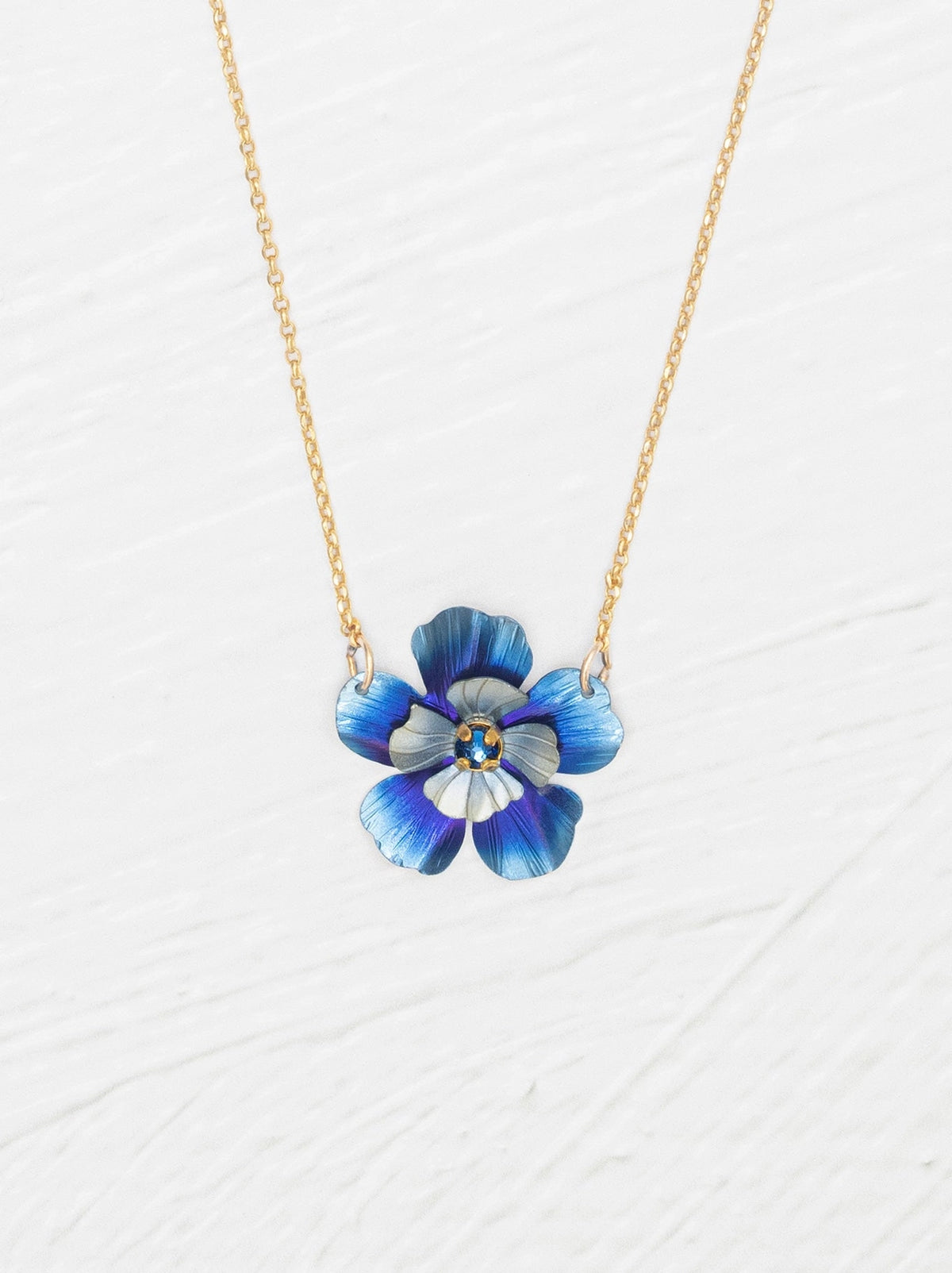 Blue flower-shaped pendant on a gold chain against a white background