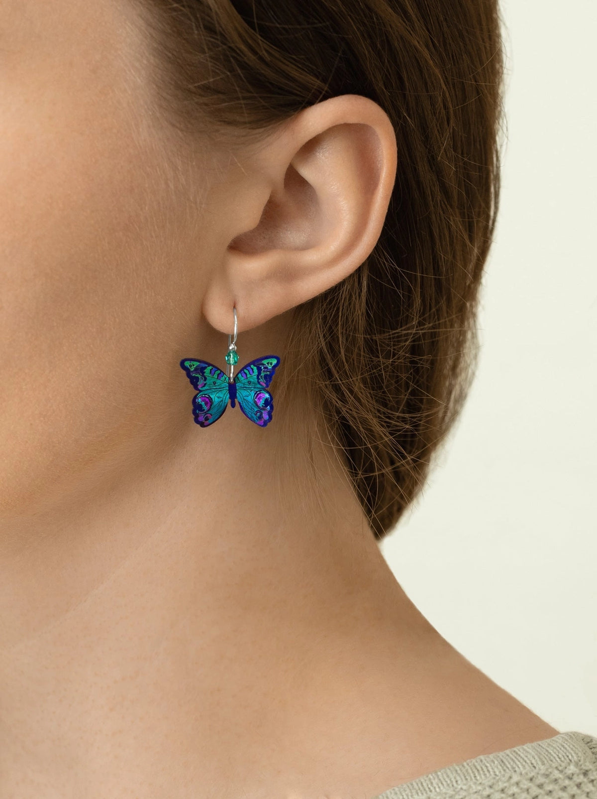 Butterfly-shaped earrings worn by a person on a neutral background