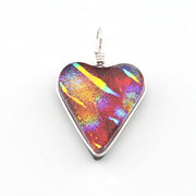 A heart-shaped glass pendant featuring a vibrant, iridescent play-of-color pattern with red, orange, yellow, and blue hues, set in a silver-colored metal bezel with a silver wire-wrapped bail on a white background.