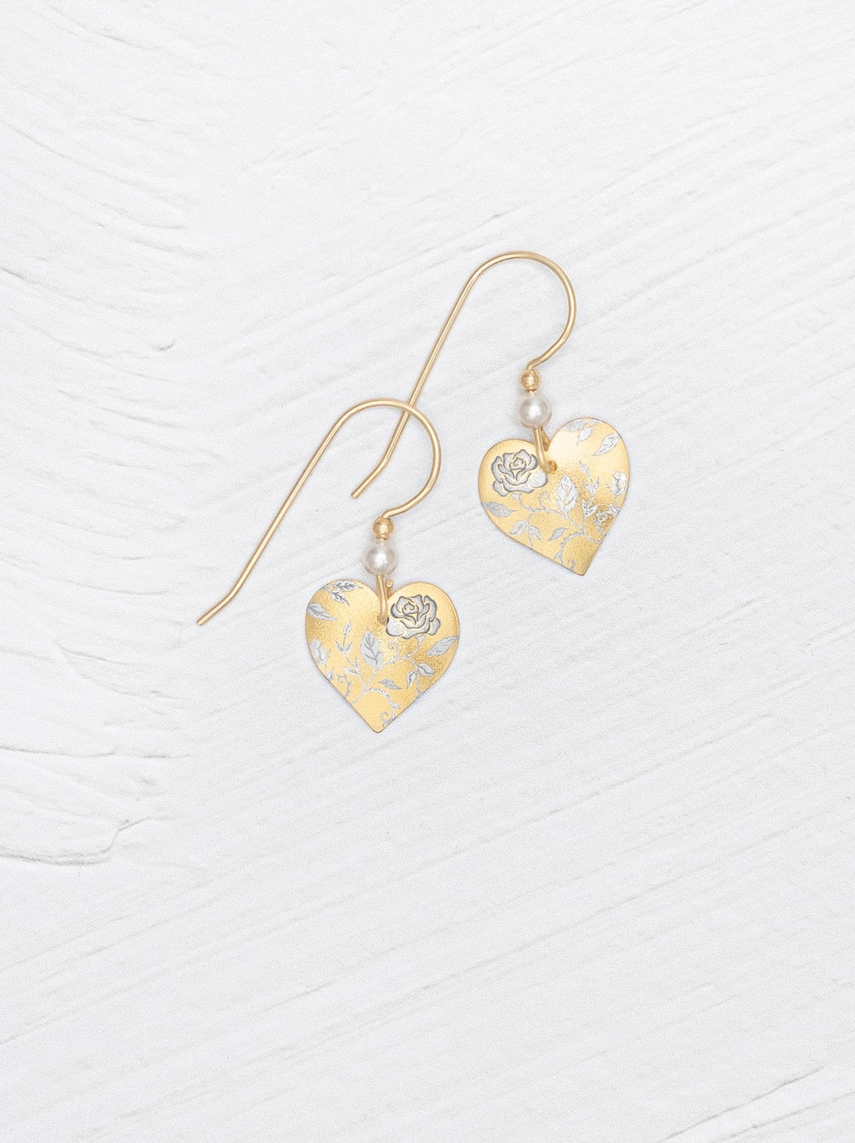 Heart-shaped gold earrings with floral details on a white background