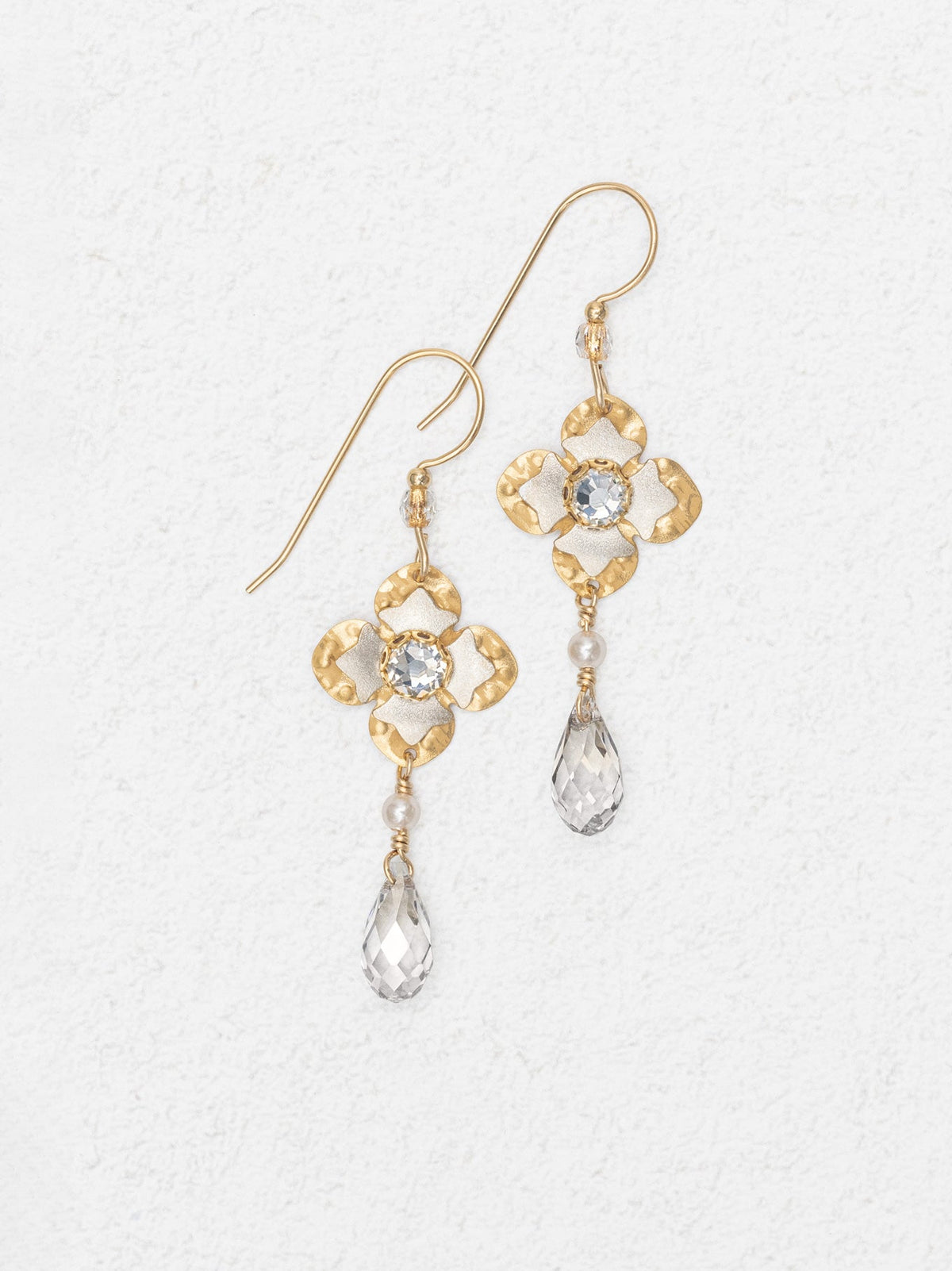 Gold earrings with floral designs and crystal-like elements on a light gray background