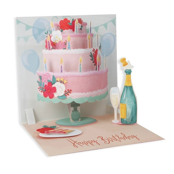 Pop-up birthday card with a three-tier cake, balloons, and champagne bottle on a white background.