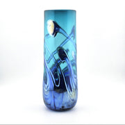 A tall, cylindrical glass vase with a vibrant blue and teal color profile, featuring abstract, fluid swirls of lighter blue, dark navy, and a small gold accent near the top, set against a plain white background.