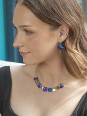 Woman wearing a colorful necklace and earrings against a blue background