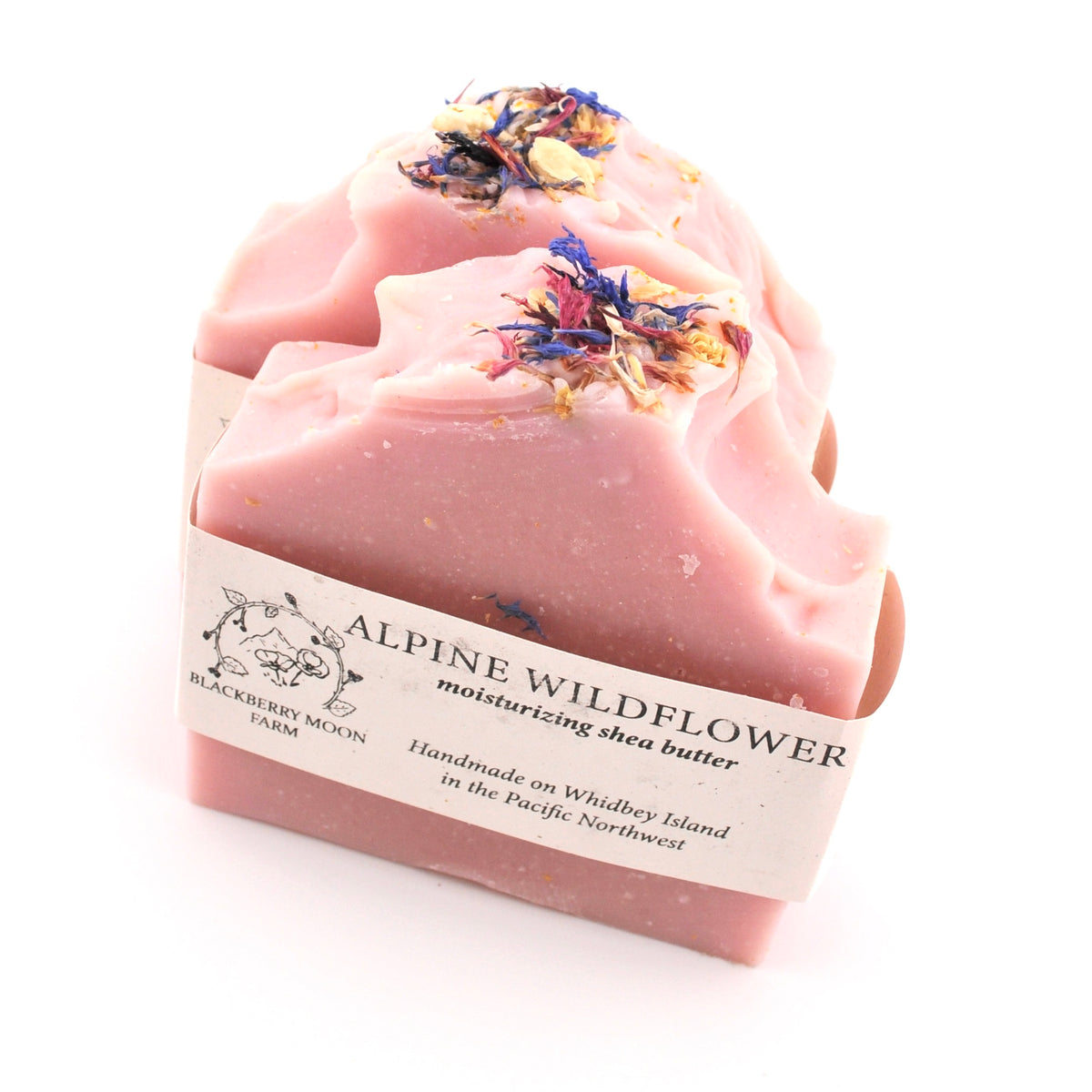 Pink soap bar with dried flowers on top and a label reading 'Alpine Wildflower' on a white background.