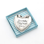 Heart-shaped silver trinket with 'You make my heart smile' text in a striped box
