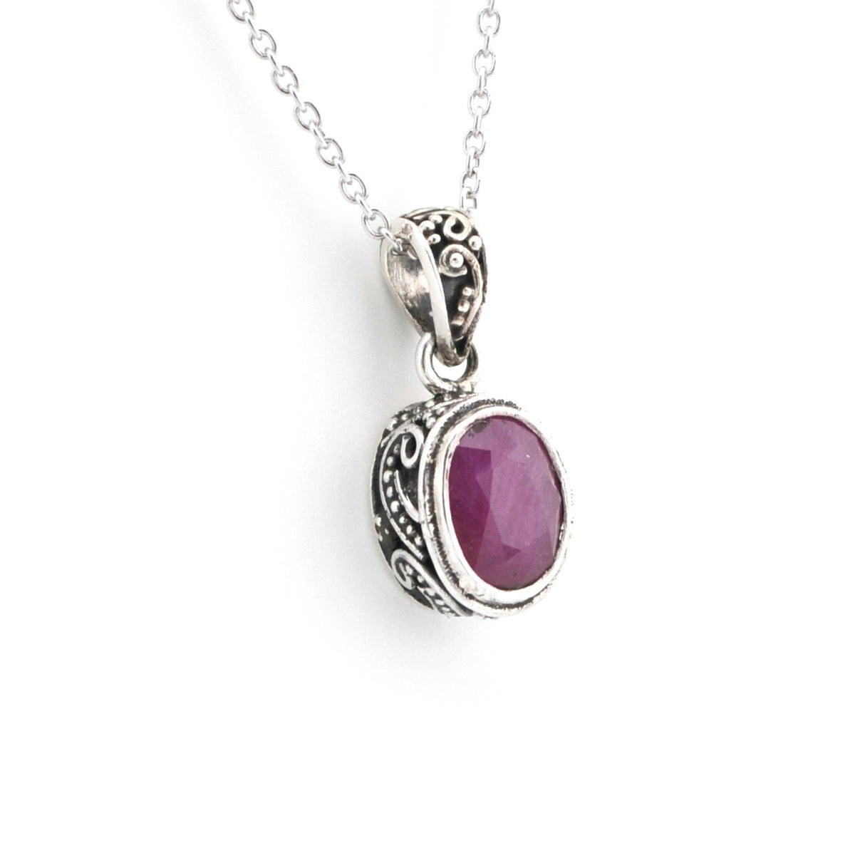 A silver pendant necklace featuring an oval purple gemstone in an ornate filigree bezel setting, suspended from a delicate silver chain against a plain white background.