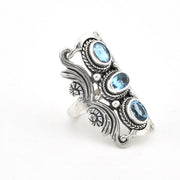 An ornate sterling silver ring featuring three oval-cut light blue gemstones, set against a plain white background.
