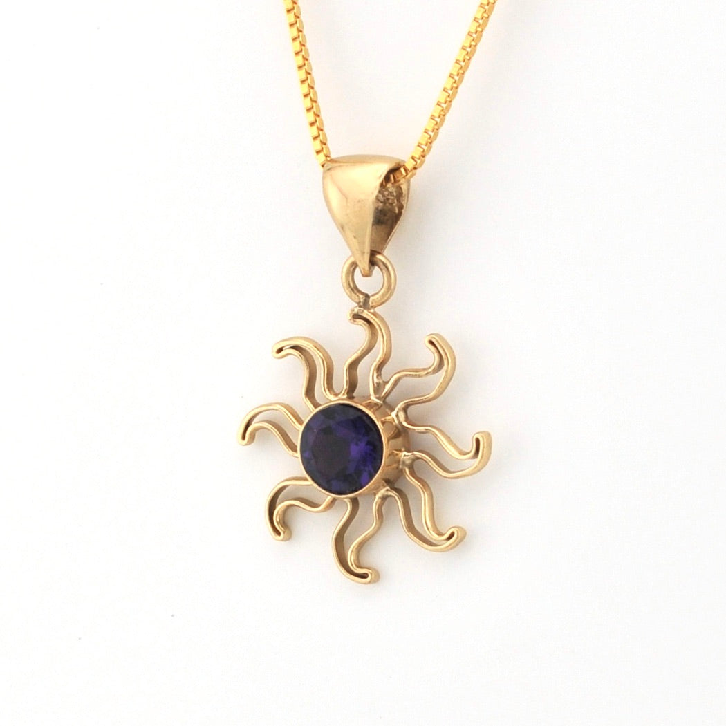 Gold sun-shaped pendant with a purple gemstone on a white background