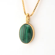 Gold necklace with a green stone pendant on a white background