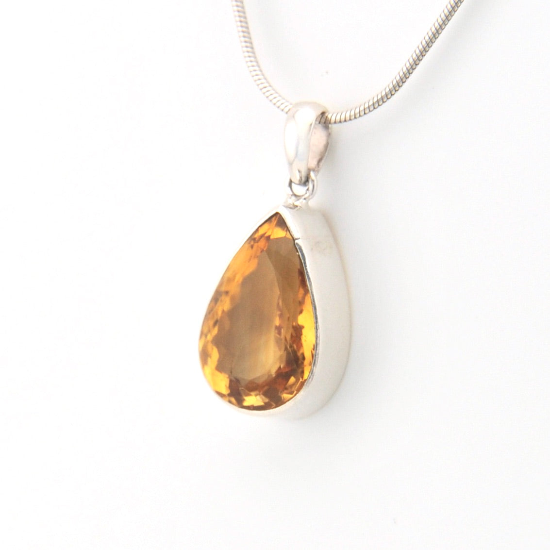 Teardrop-shaped citrine pendant on a silver chain against a white background