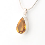 Teardrop-shaped citrine pendant on a silver chain against a white background