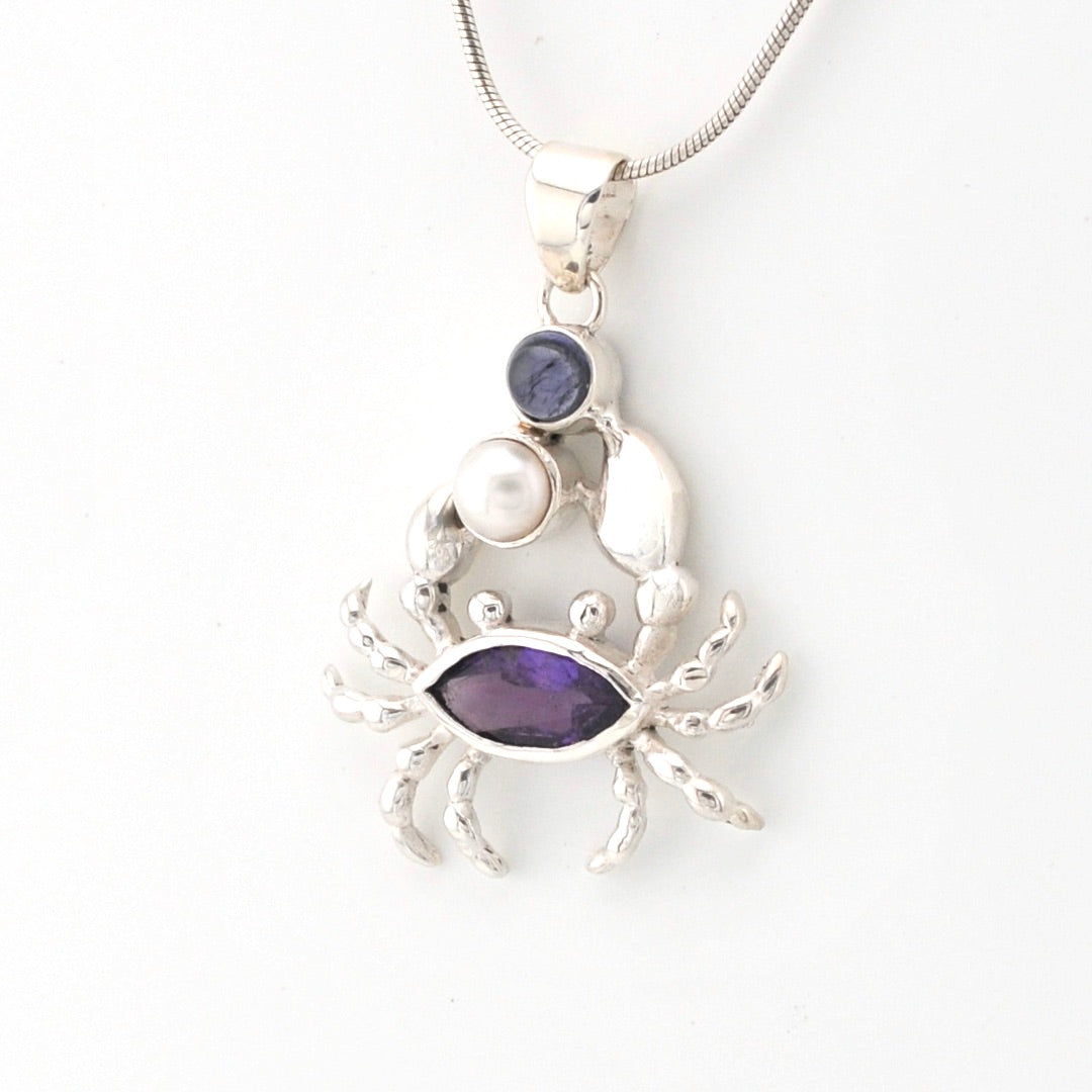 Silver crab pendant with purple gemstones on a white background