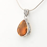 Teardrop-shaped citrine pendant on a silver chain against a white background