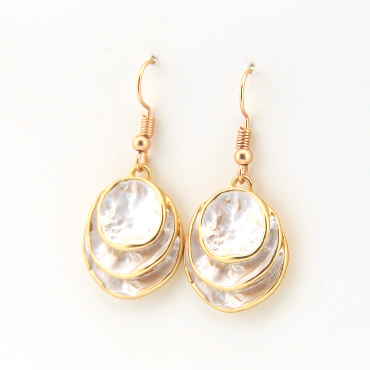 Gold and white layered earrings on a white background