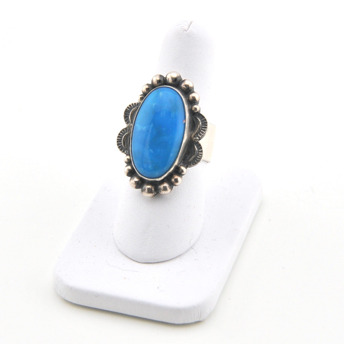 Blue stone ring with silver decorative band on a white stand