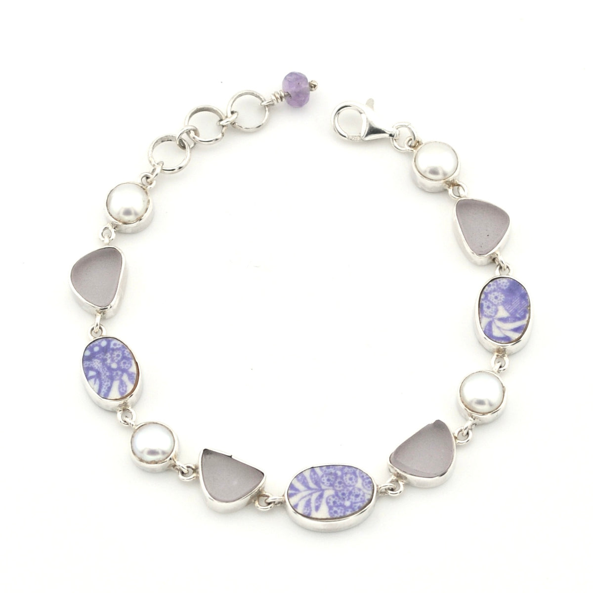 A silver link bracelet featuring alternating round white pearls, smooth light gray teardrop-shaped stones, and oval and marquise-cut lavender and white porcelain, shown on a plain white background.