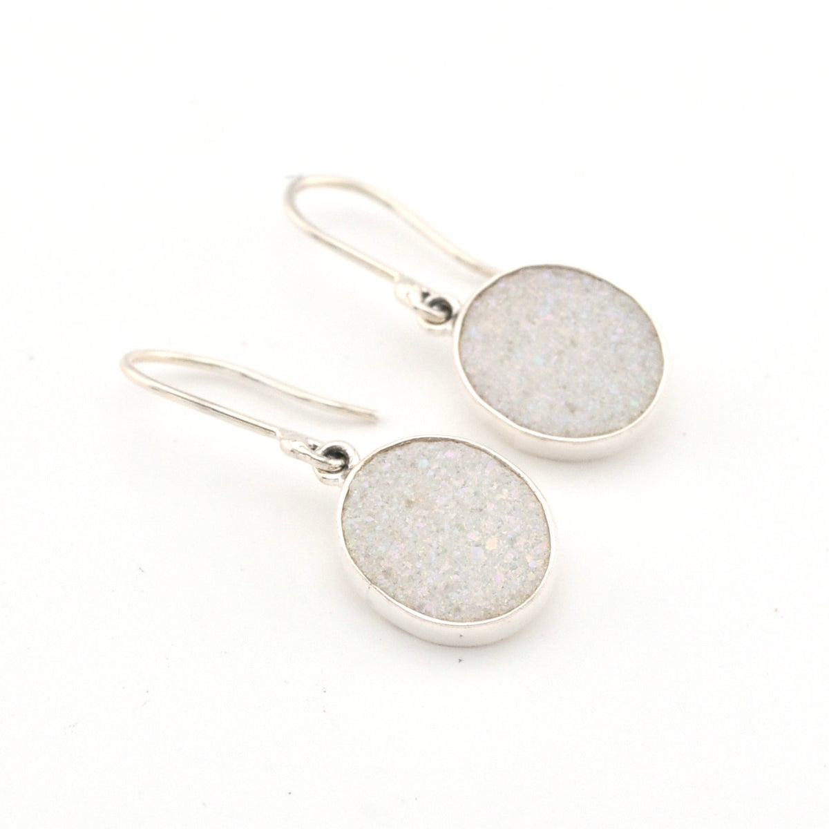 Pair of silver earrings with round, light gray stone drops on a white background