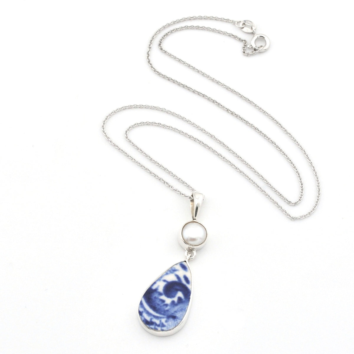 A silver chain necklace featuring a teardrop-shaped pendant with a blue and white marbled pattern, accented by a small round white pearl, shown on a plain white background.