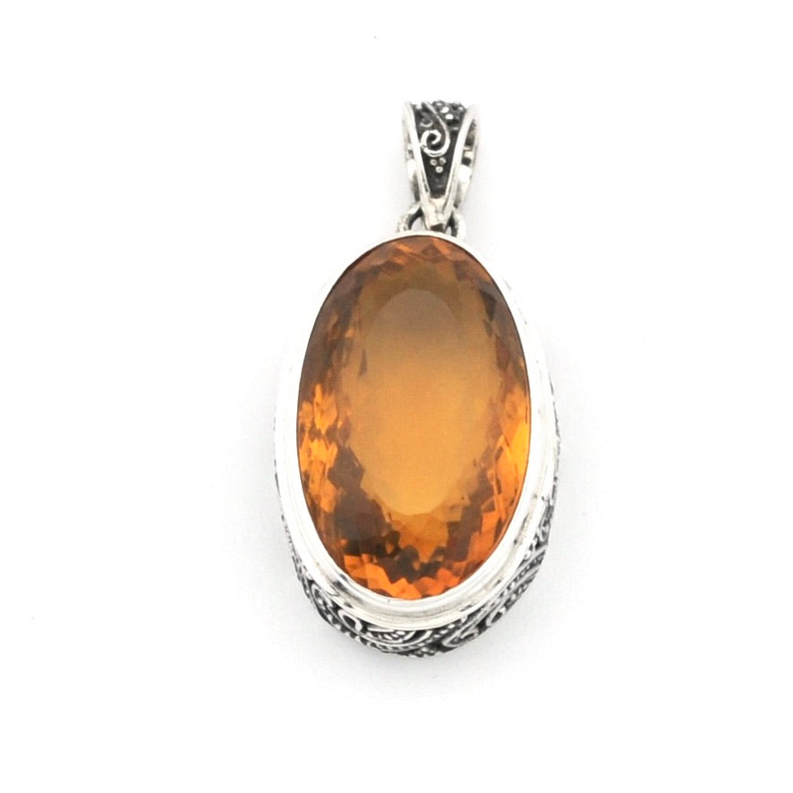 A silver pendant featuring a large, oval-shaped amber-orange gemstone, set in a textured silver bezel with a decorative bail at the top, shown against a plain white background.