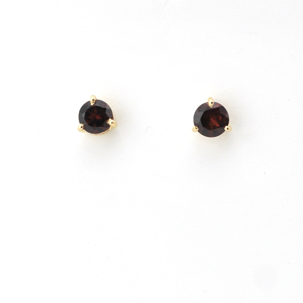 Pair of gold earrings with round dark gemstones on a white background